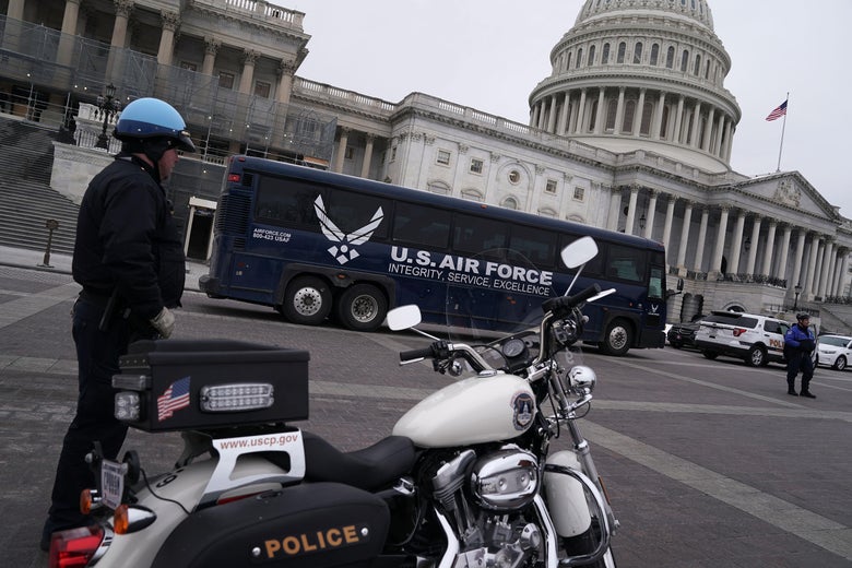 A blue U.S. Air Force bus in front of the Capitol. A police officer stands by his motorcycle in the foreground.
